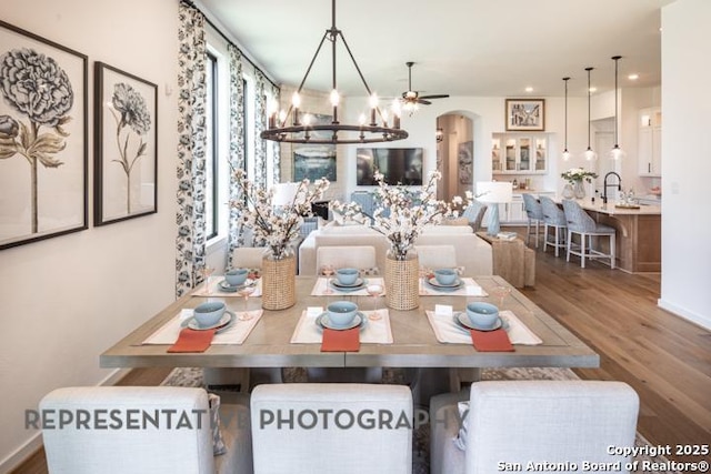 dining area featuring arched walkways, a notable chandelier, wood finished floors, and recessed lighting