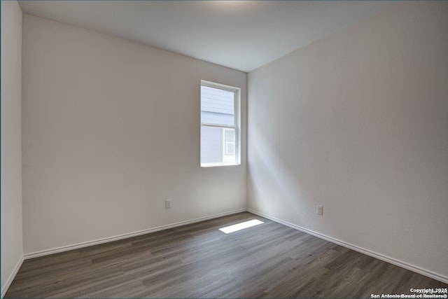 spare room featuring baseboards and dark wood-style flooring