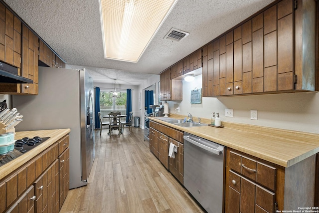 kitchen featuring a textured ceiling, dishwasher, a sink, light countertops, and light wood-style flooring