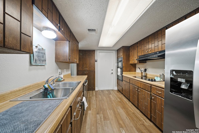 kitchen with visible vents, under cabinet range hood, a sink, light wood finished floors, and black appliances