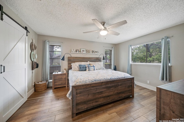 bedroom featuring baseboards, a barn door, a textured ceiling, and hardwood / wood-style floors