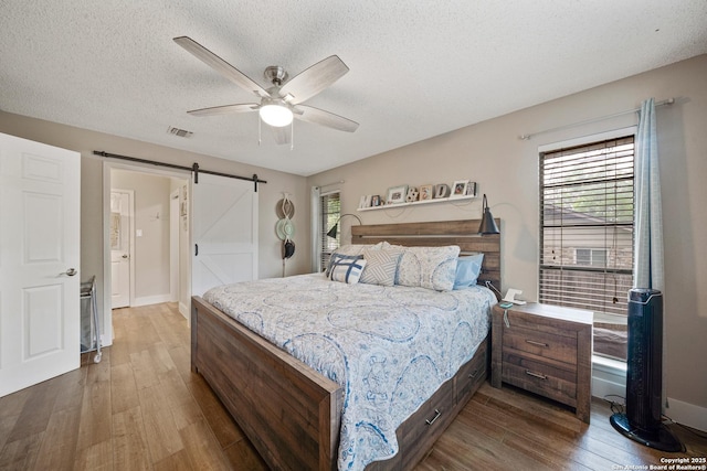 bedroom featuring a barn door, a textured ceiling, baseboards, wood finished floors, and visible vents