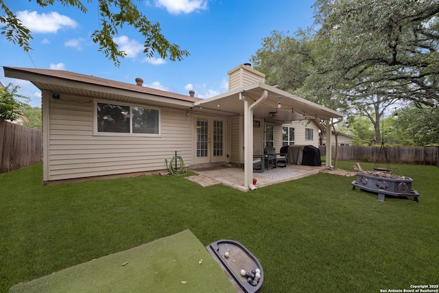 rear view of house featuring french doors, a lawn, a patio area, a fenced backyard, and a fire pit
