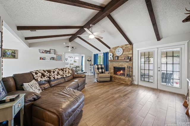 living room with a ceiling fan, a textured ceiling, a brick fireplace, wood finished floors, and lofted ceiling with beams