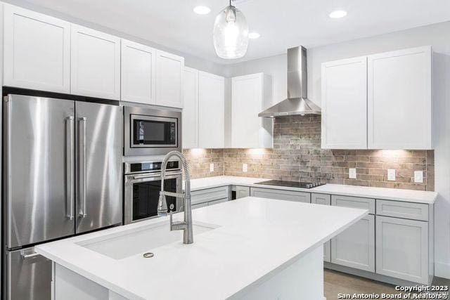 kitchen featuring wall chimney range hood, light countertops, stainless steel appliances, and a sink