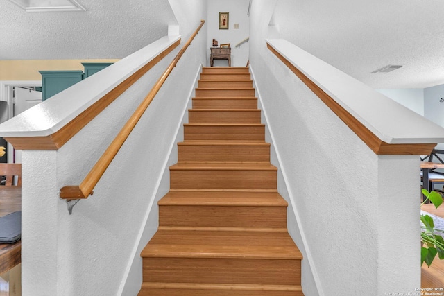 stairs with a textured wall, a textured ceiling, and visible vents