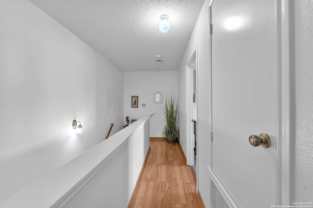corridor with light wood-type flooring, a textured ceiling, and an upstairs landing
