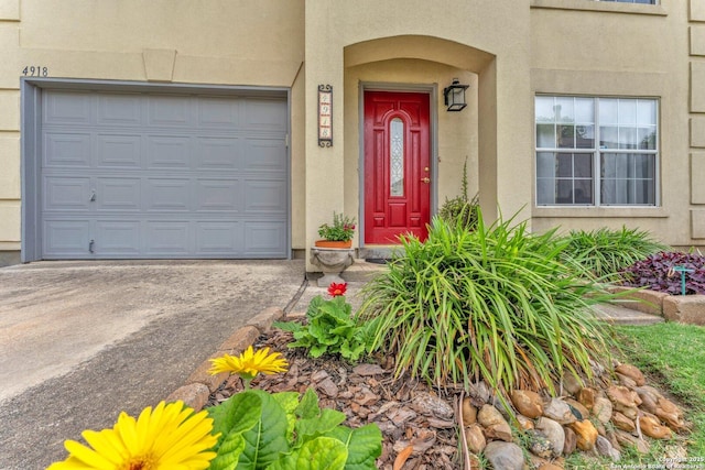 entrance to property featuring a garage, stucco siding, and driveway