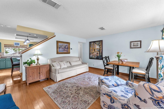 living area with visible vents, light wood-style flooring, and a textured ceiling
