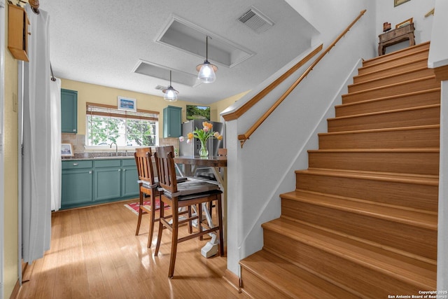 staircase with a textured ceiling, attic access, wood finished floors, and visible vents