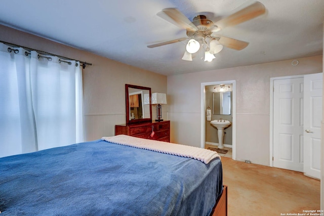bedroom with a sink, ensuite bathroom, ceiling fan, and light colored carpet