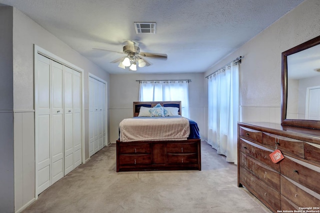 carpeted bedroom with two closets, a textured ceiling, ceiling fan, and visible vents