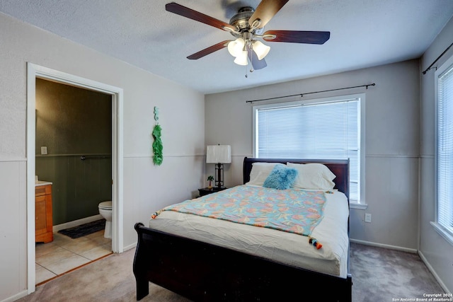 bedroom featuring light colored carpet, ceiling fan, and ensuite bath