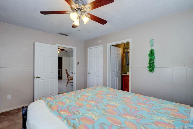 bedroom with a wainscoted wall, a ceiling fan, a textured ceiling, and visible vents