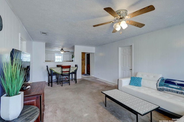 living room featuring a ceiling fan, a textured ceiling, visible vents, and light carpet