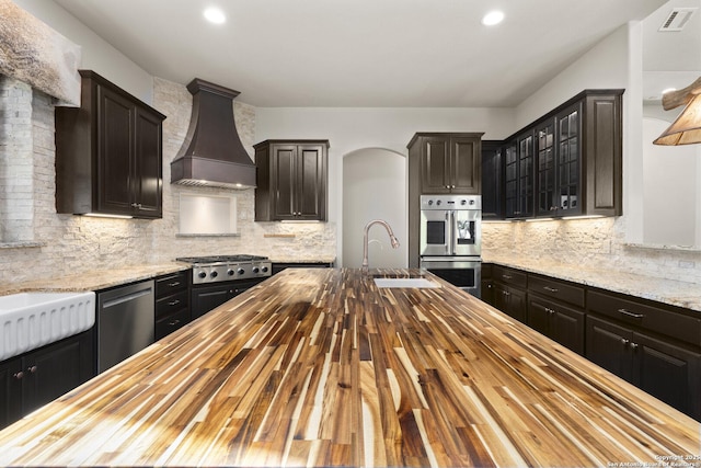 kitchen featuring visible vents, appliances with stainless steel finishes, a sink, premium range hood, and wood counters