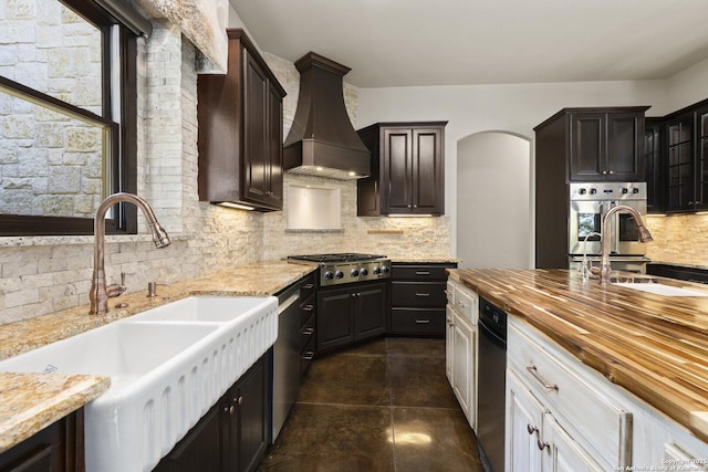 kitchen featuring backsplash, appliances with stainless steel finishes, a sink, premium range hood, and wood counters