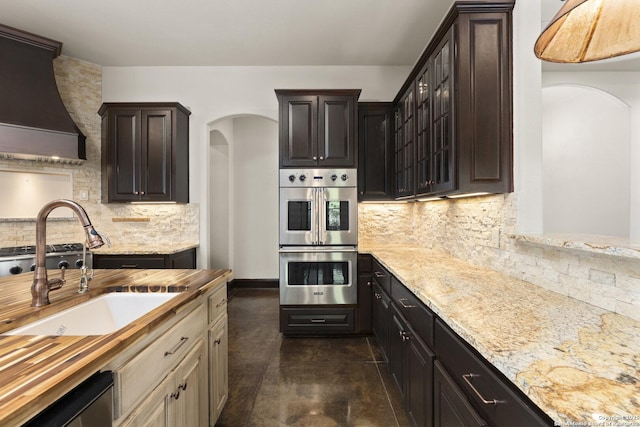 kitchen featuring backsplash, stainless steel double oven, arched walkways, a sink, and butcher block counters