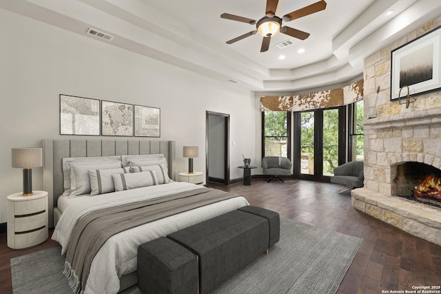 bedroom featuring a tray ceiling, dark wood-type flooring, a stone fireplace, and visible vents
