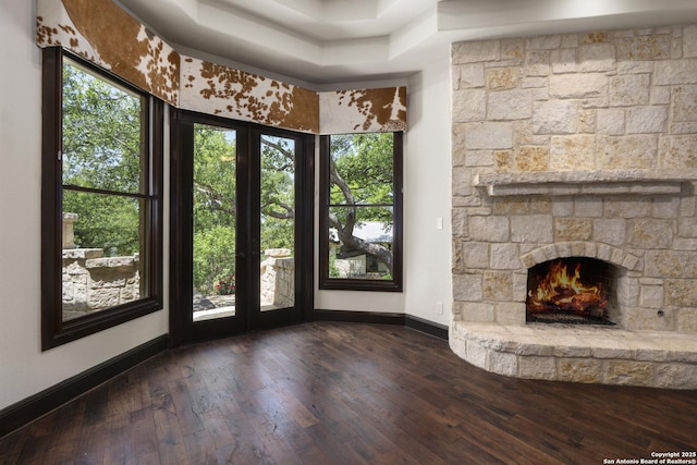 unfurnished living room with dark wood-style flooring, baseboards, and a stone fireplace