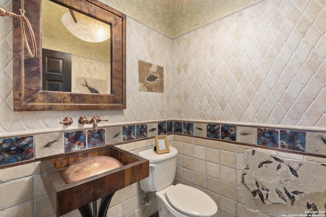 bathroom with a sink, wainscoting, toilet, and tile walls