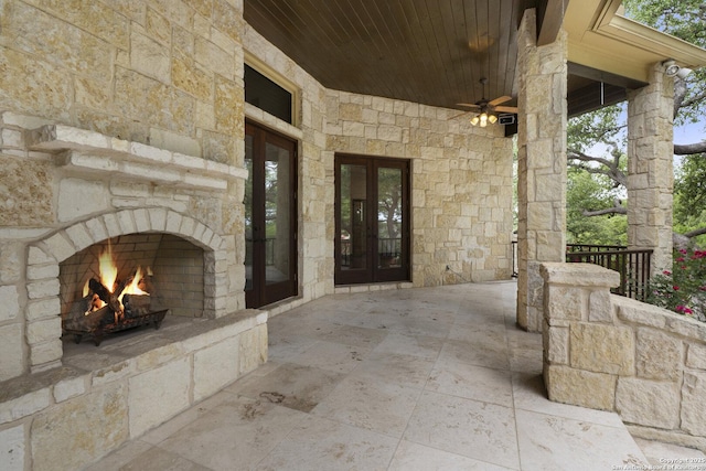 view of patio / terrace featuring an outdoor stone fireplace, a ceiling fan, and french doors