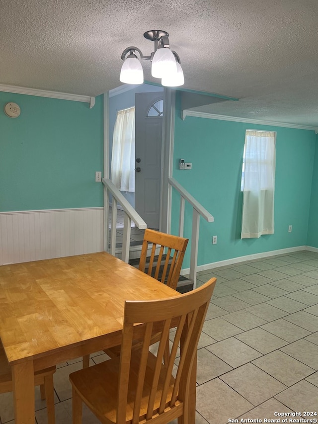 dining space with wainscoting, ornamental molding, light tile patterned flooring, and a textured ceiling
