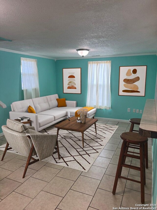 living area featuring baseboards, ornamental molding, a textured ceiling, and light tile patterned flooring