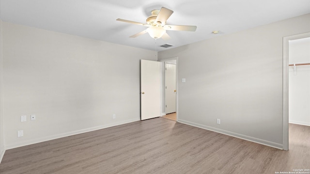 unfurnished bedroom with baseboards, a walk in closet, visible vents, and wood finished floors
