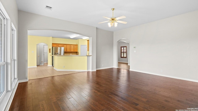 unfurnished living room featuring arched walkways, hardwood / wood-style floors, a ceiling fan, baseboards, and visible vents