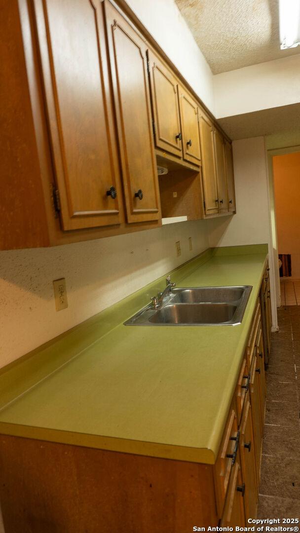 kitchen with dark tile patterned floors, a sink, a textured ceiling, and brown cabinets