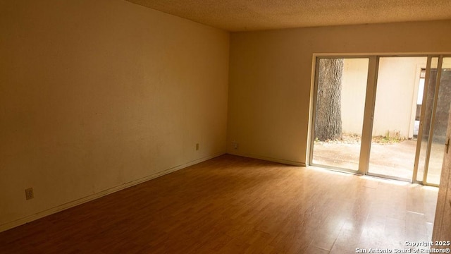 spare room featuring baseboards, a textured ceiling, and wood finished floors
