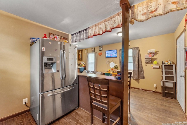 kitchen featuring baseboards, wood finished floors, and stainless steel fridge with ice dispenser