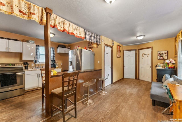 kitchen featuring a breakfast bar, a textured ceiling, light wood-style flooring, stainless steel appliances, and white cabinetry