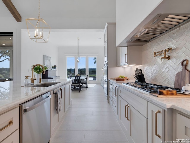 kitchen featuring a sink, a chandelier, wall chimney exhaust hood, stainless steel appliances, and backsplash