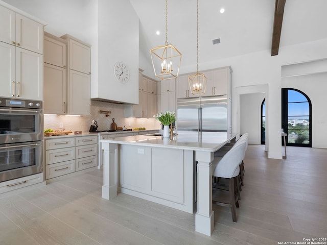 kitchen with decorative backsplash, light countertops, high vaulted ceiling, an inviting chandelier, and stainless steel appliances