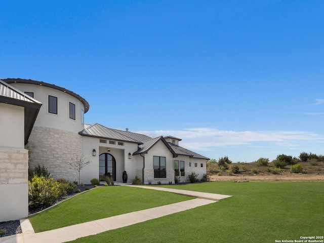 view of front of home with a front lawn, stone siding, stucco siding, a standing seam roof, and metal roof