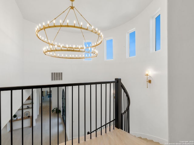 stairway featuring a high ceiling, a notable chandelier, baseboards, and visible vents