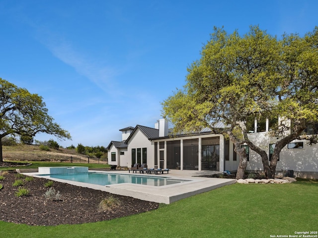 rear view of house with a chimney, an outdoor pool, a sunroom, a yard, and a patio