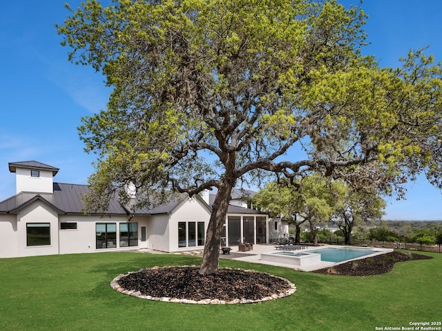 back of property featuring stucco siding, a sunroom, an outdoor pool, a standing seam roof, and a lawn