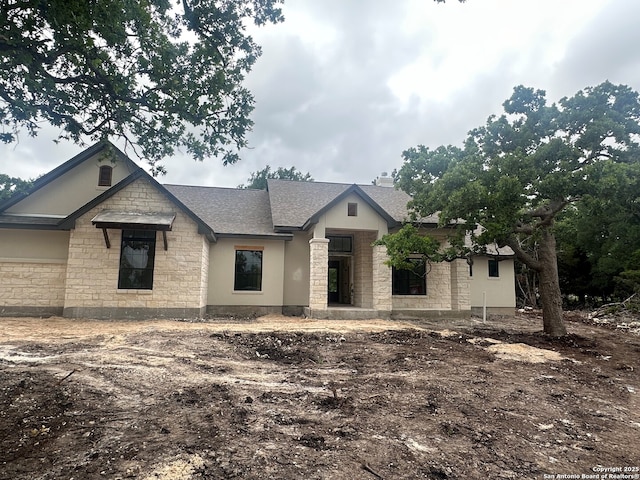 view of front facade with roof with shingles, stucco siding, a garage, and stone siding