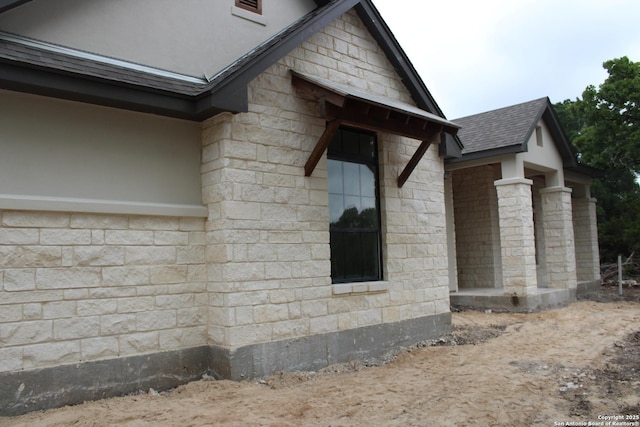 view of side of property with a shingled roof and stone siding