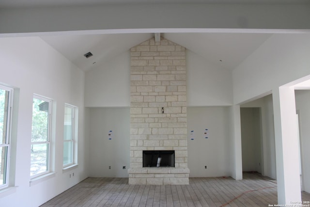 unfurnished living room featuring high vaulted ceiling, light wood-type flooring, beam ceiling, and a fireplace