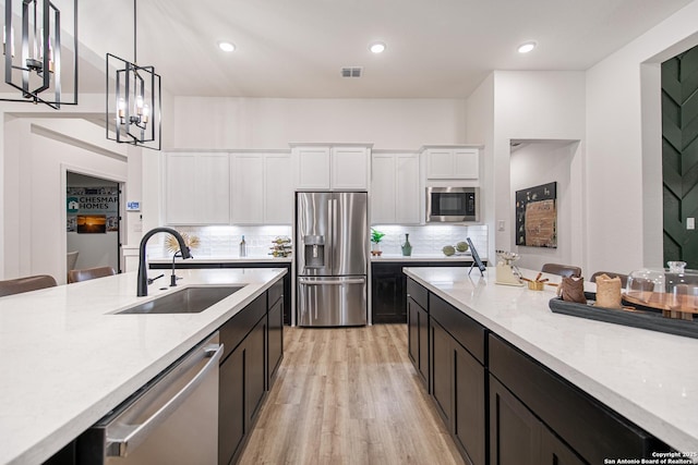 kitchen with pendant lighting, white cabinetry, a sink, stainless steel appliances, and light wood-style flooring