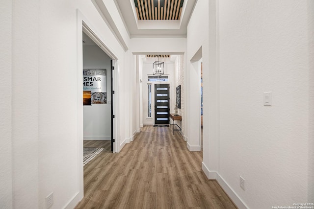 corridor featuring baseboards, a chandelier, wood finished floors, and visible vents
