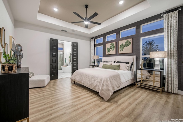 bedroom featuring light wood finished floors, a raised ceiling, ensuite bath, recessed lighting, and visible vents