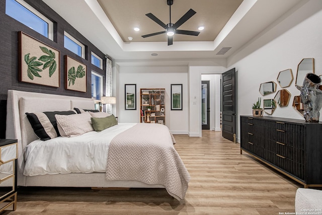 bedroom with visible vents, light wood-type flooring, baseboards, a tray ceiling, and recessed lighting