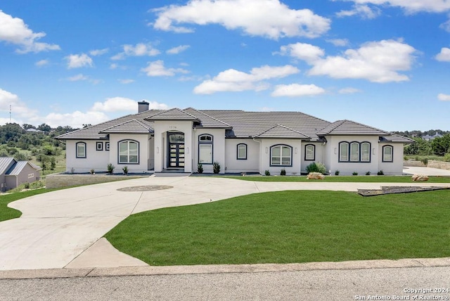 view of front of home featuring curved driveway, a chimney, stucco siding, and a front lawn