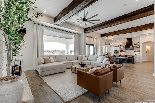 living room with light wood-style flooring, plenty of natural light, beam ceiling, and ceiling fan with notable chandelier