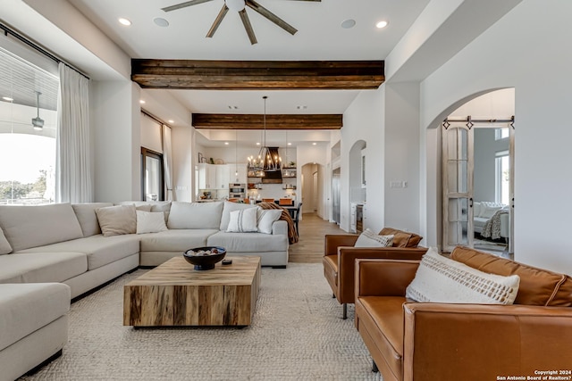 living area featuring plenty of natural light, arched walkways, ceiling fan with notable chandelier, and beamed ceiling
